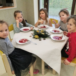 pokaż obrazek - Zdjęcie przedstawia grupę dzieci spożywającą uroczystą Wigilię.
