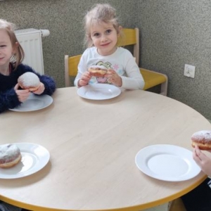 pokaż obrazek - Zdjęcie przedstawia grupę dzieci jedzących smaczne pączki.